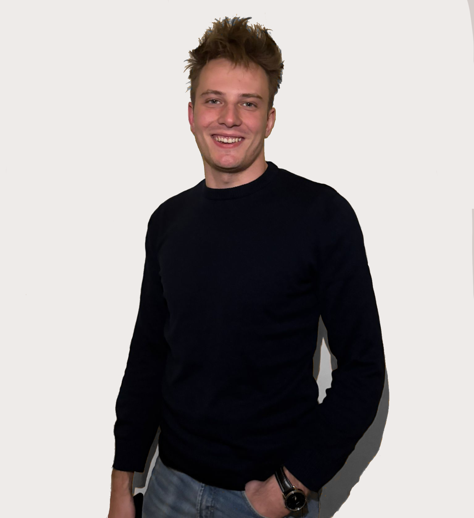 zdjęcie blondyna na miałym tle stojący w granatowym swetrze z ręką w kieszeni